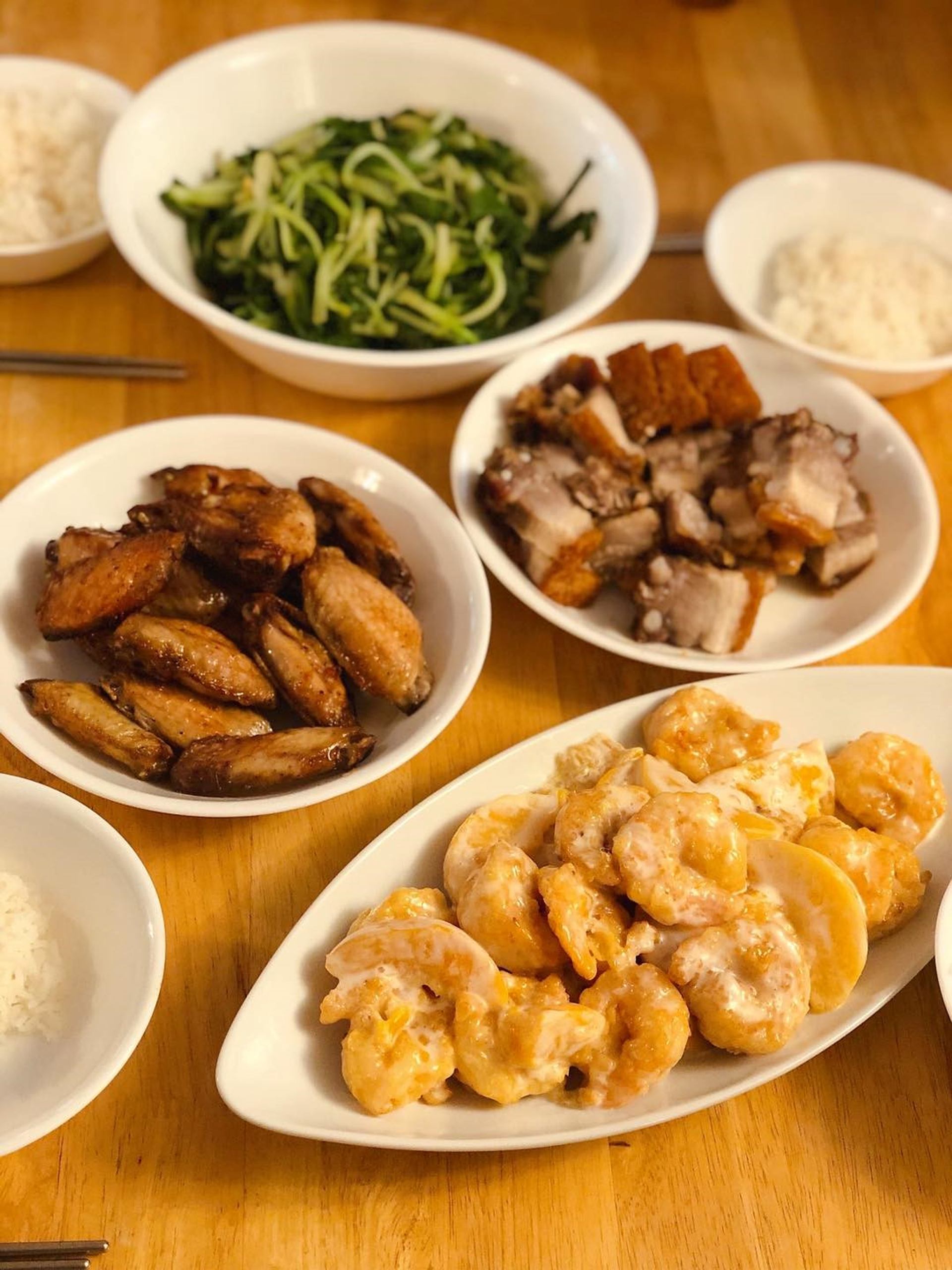 Assorted Chinese dishes on a wooden table, including crispy pork, chicken wings, vegetables, and rice.