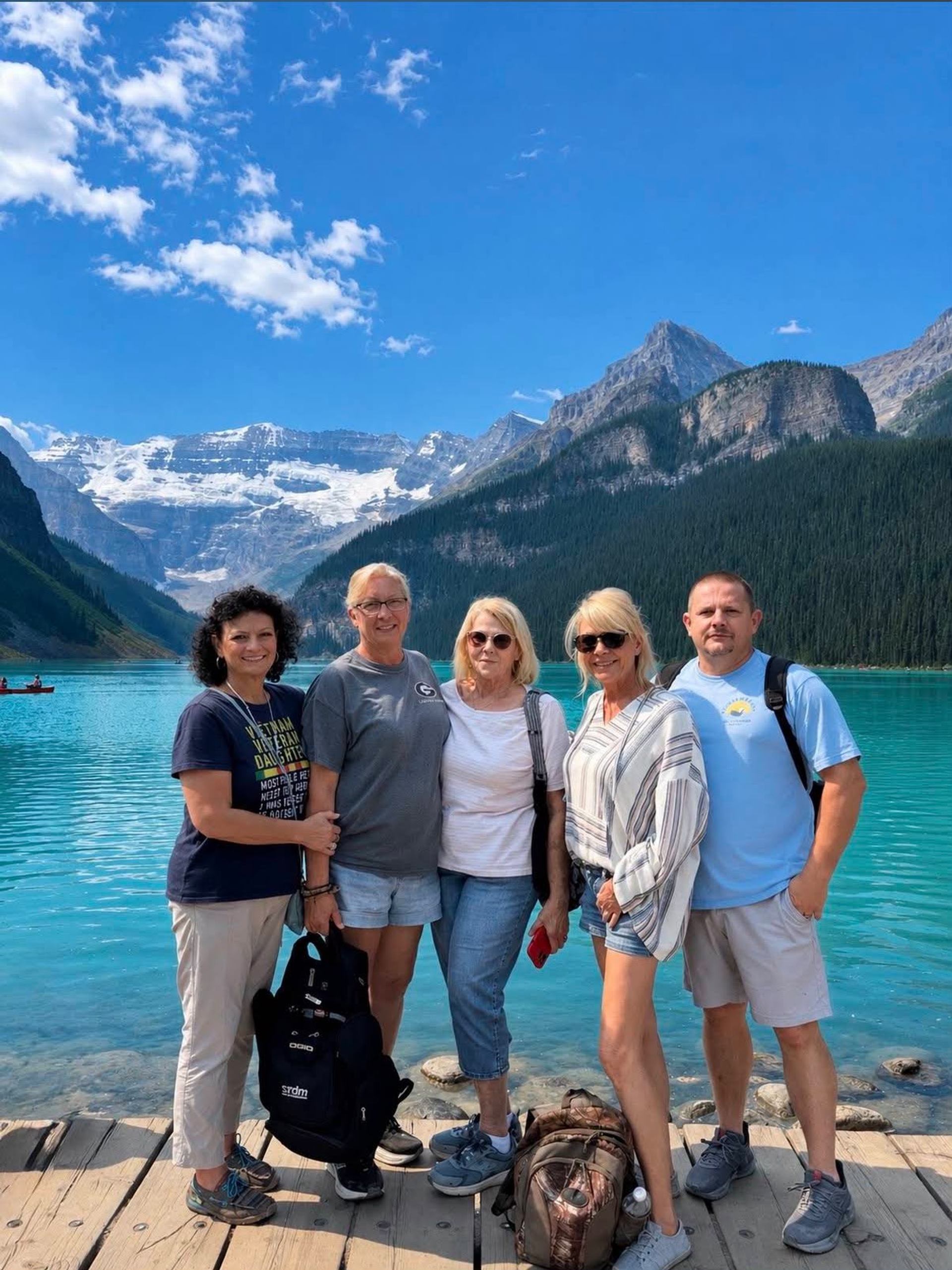 Group poses on a dock beside a turquoise lake and snow-capped mountains.