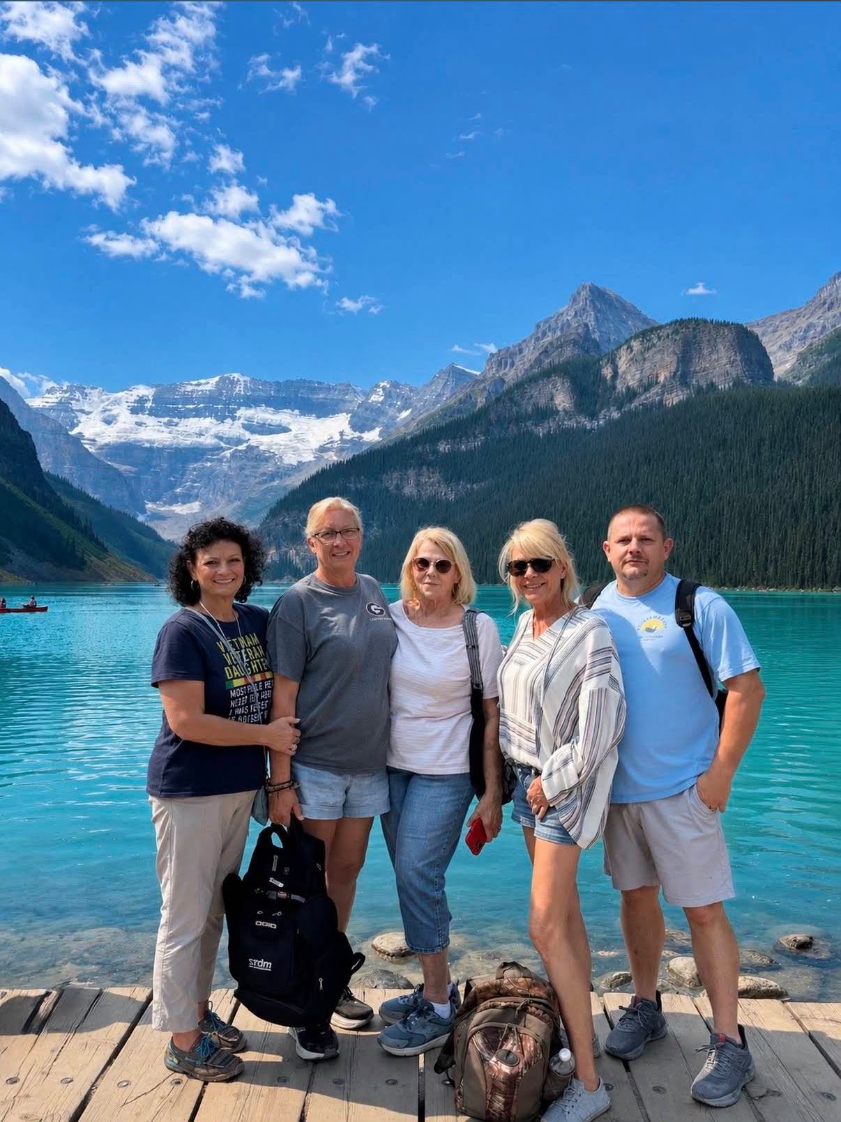 Group poses on a dock beside a turquoise lake and snow-capped mountains.