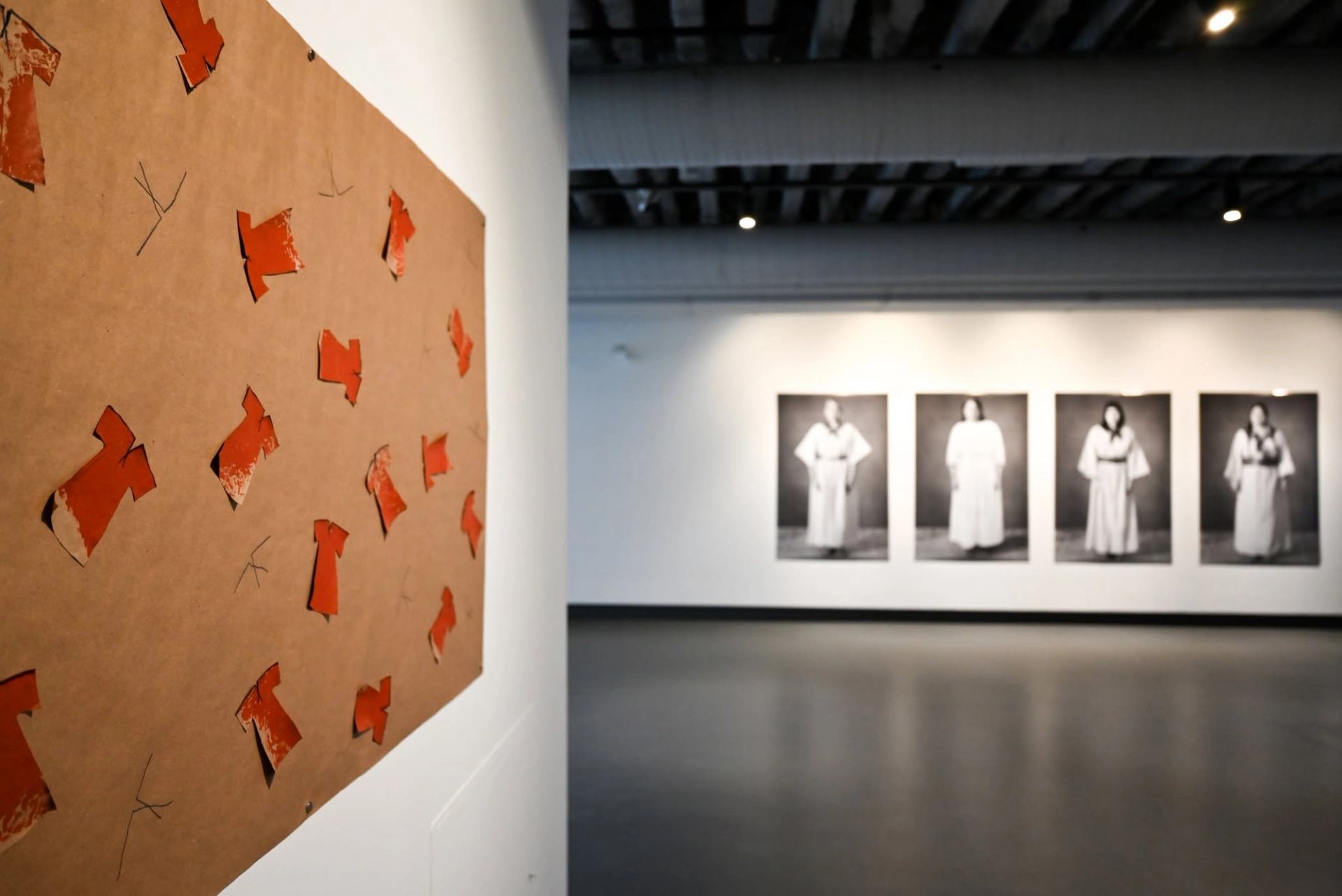 Art gallery wall with red paper dress cutouts and blurred portraits in robes.