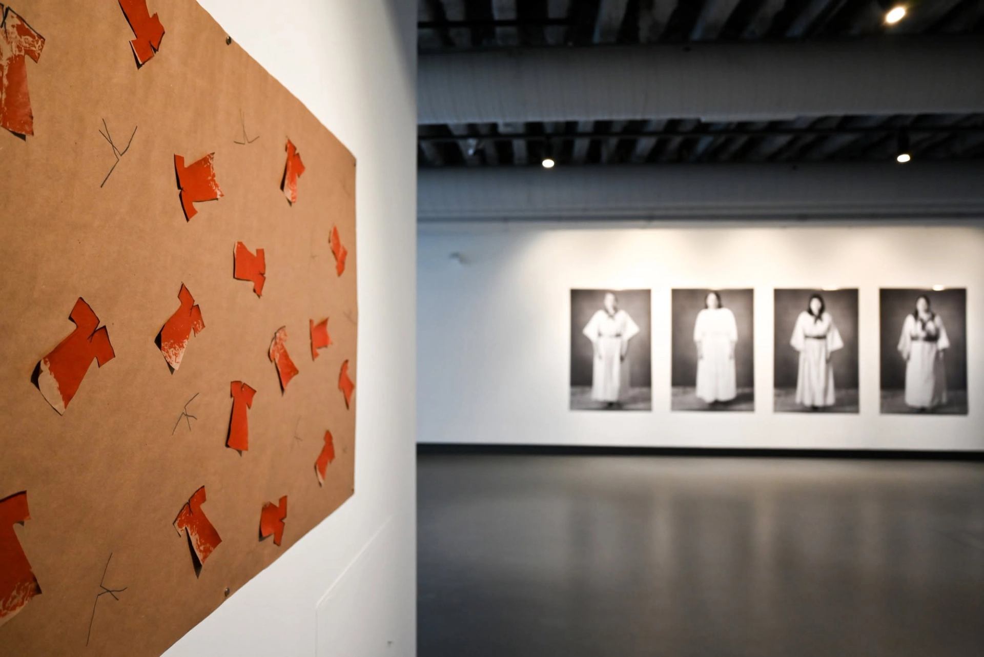 Art gallery wall with red paper dress cutouts and blurred portraits in robes.