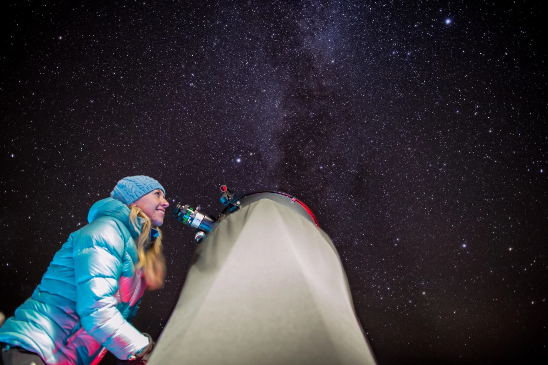 Person looking through a telescope under a clear, star-filled night sky.