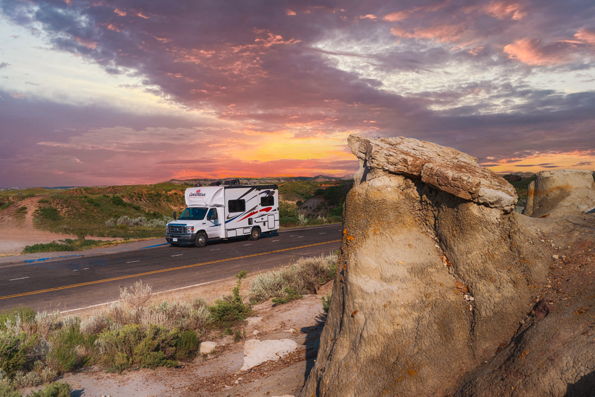 CanaDream RV driving through desert at sunset with vibrant sky and rock formations.