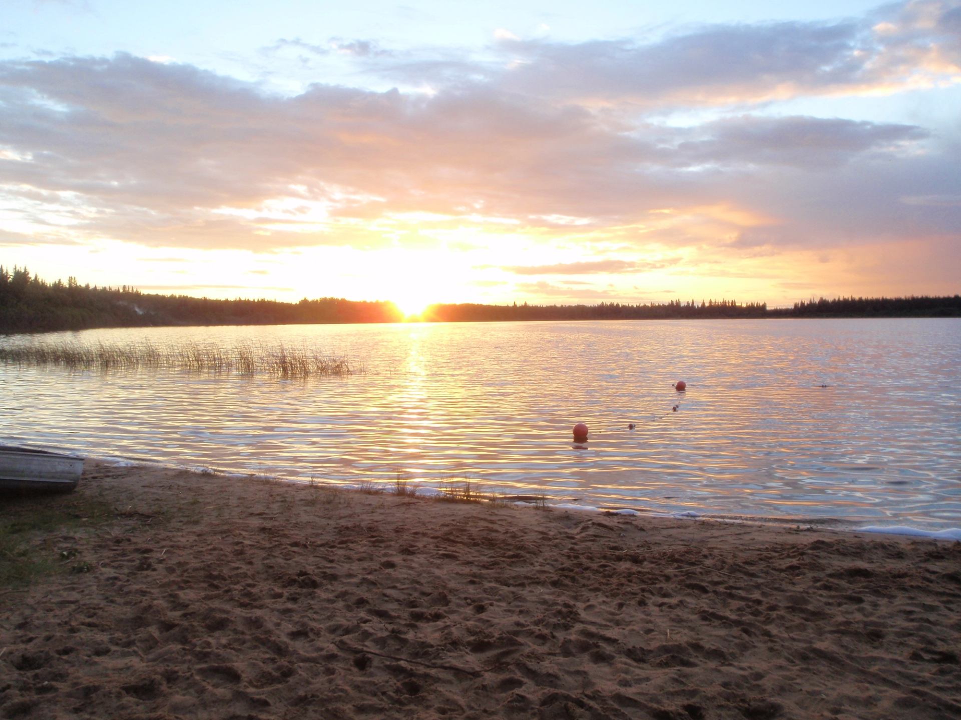 Sandy beach at sunset with calm lake water and glowing sky.