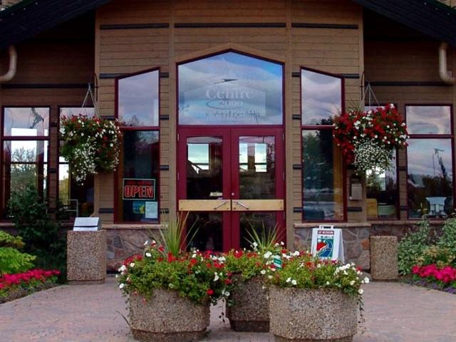 Building entrance with red doors, flower pots, and hanging baskets.