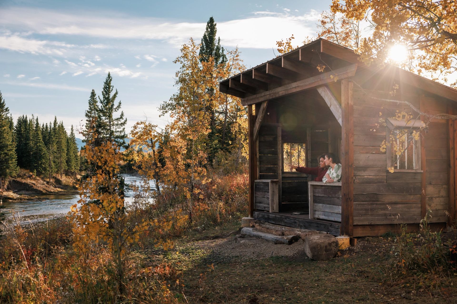 Rustic cabin by river with autumn trees at River Retreat Kananaskis.