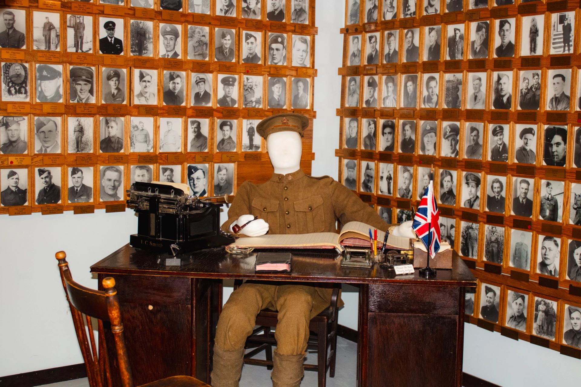War-themed exhibit at Millet Museum with uniformed mannequin and wall of soldier portraits.