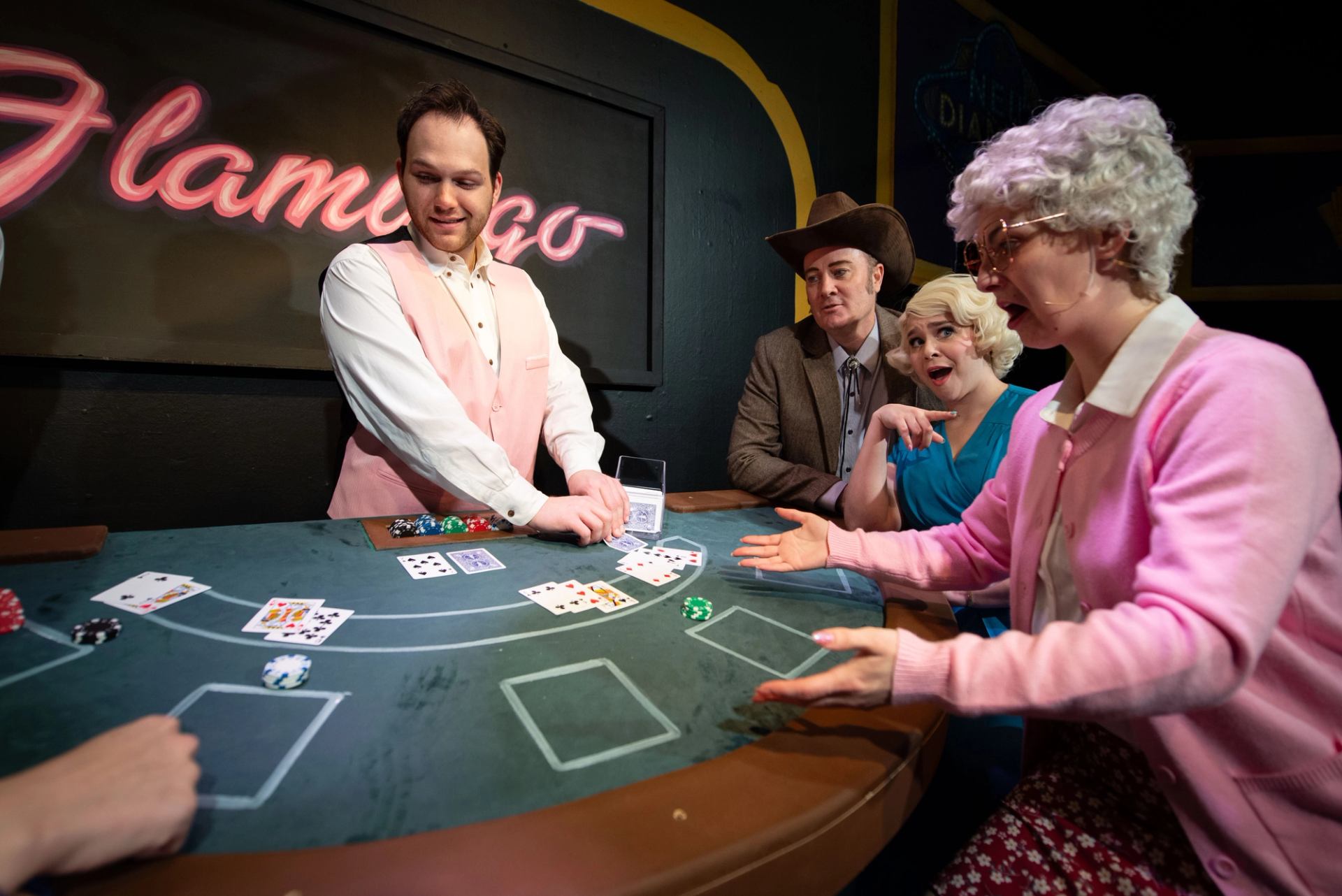 Casino dealer in pink vest deals cards to three players at blackjack table.