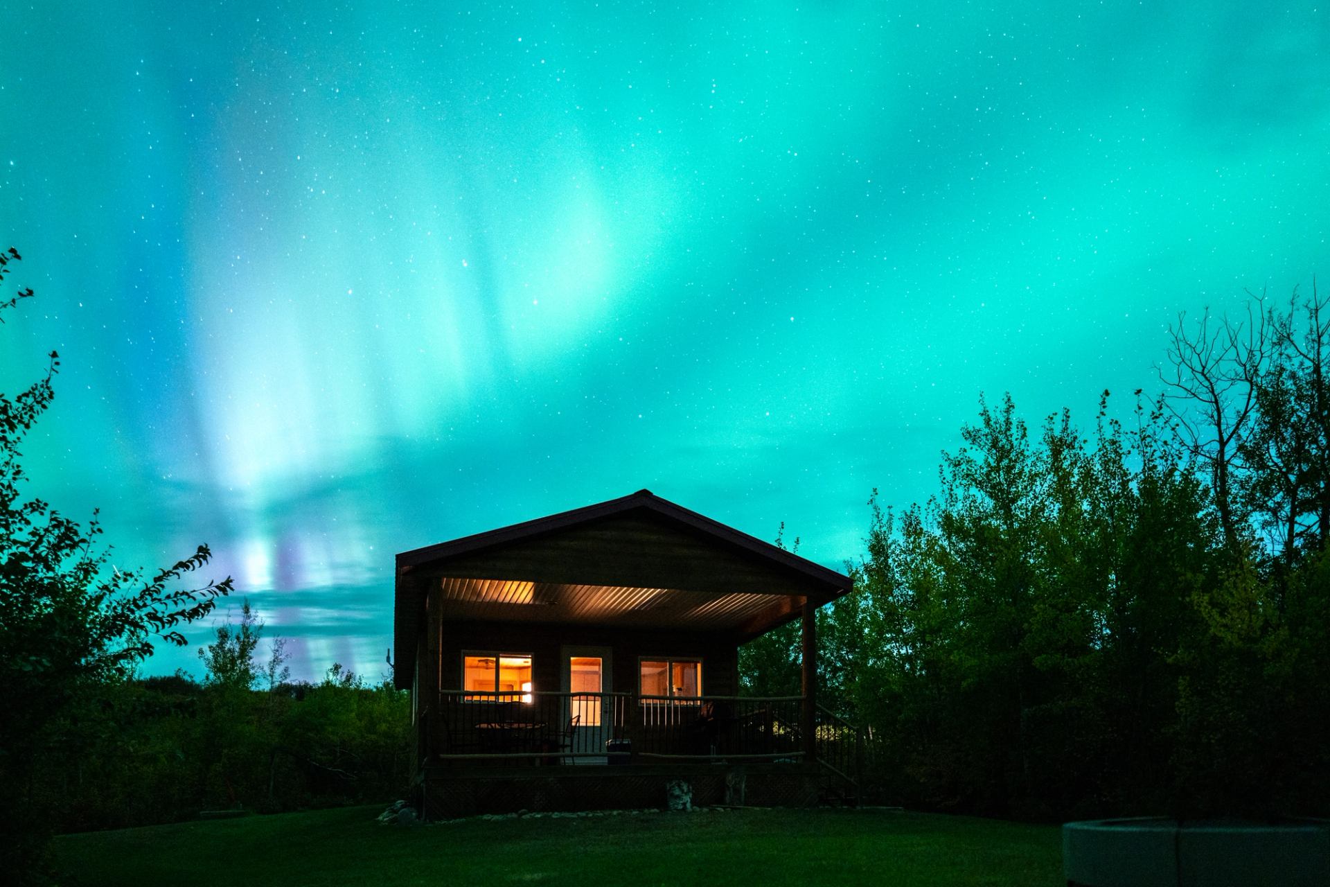 Peace River cabin glowing beneath green and blue aurora borealis sky.