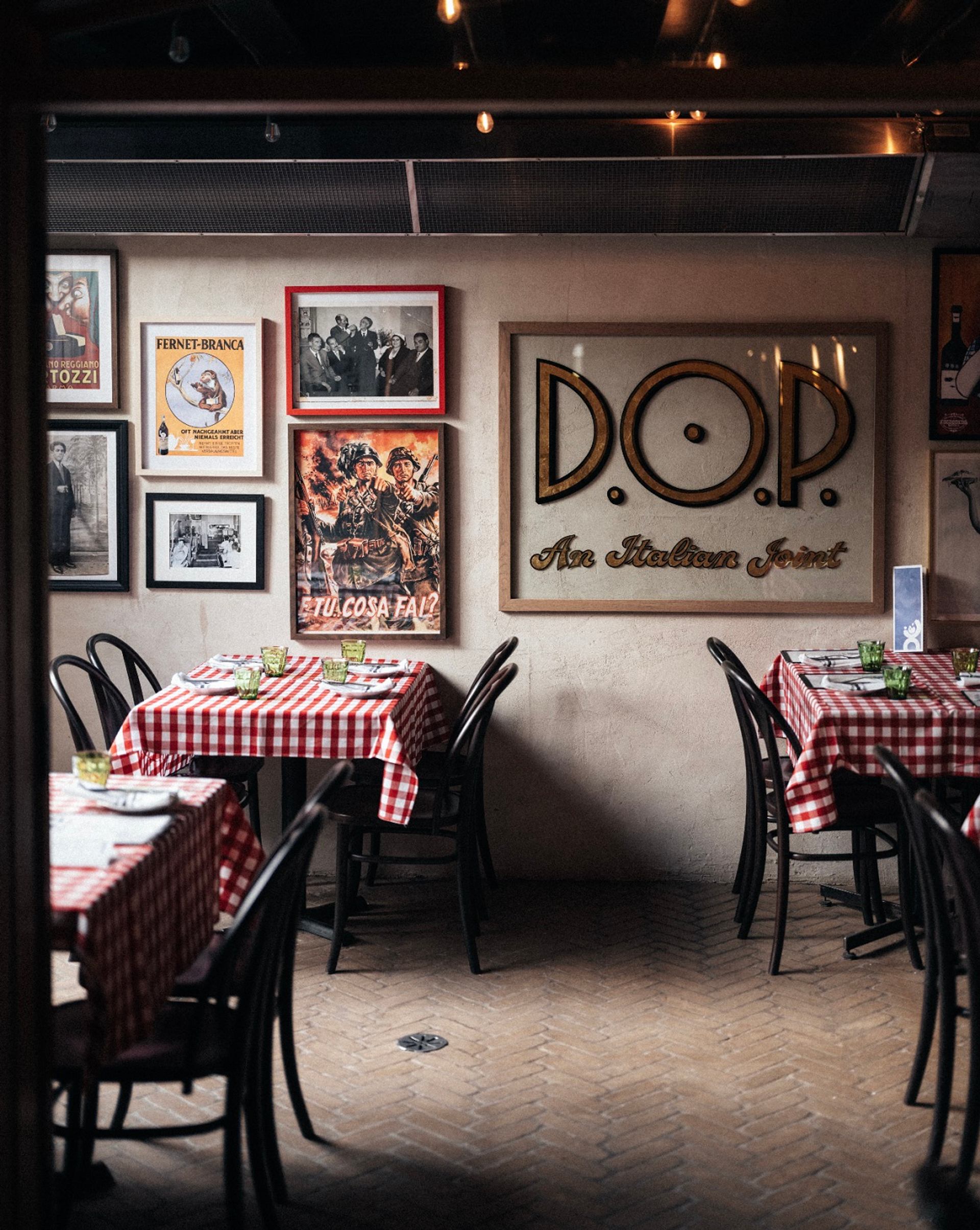 Italian restaurant interior with checkered tablecloths, framed posters and D.O.P. wall sign.