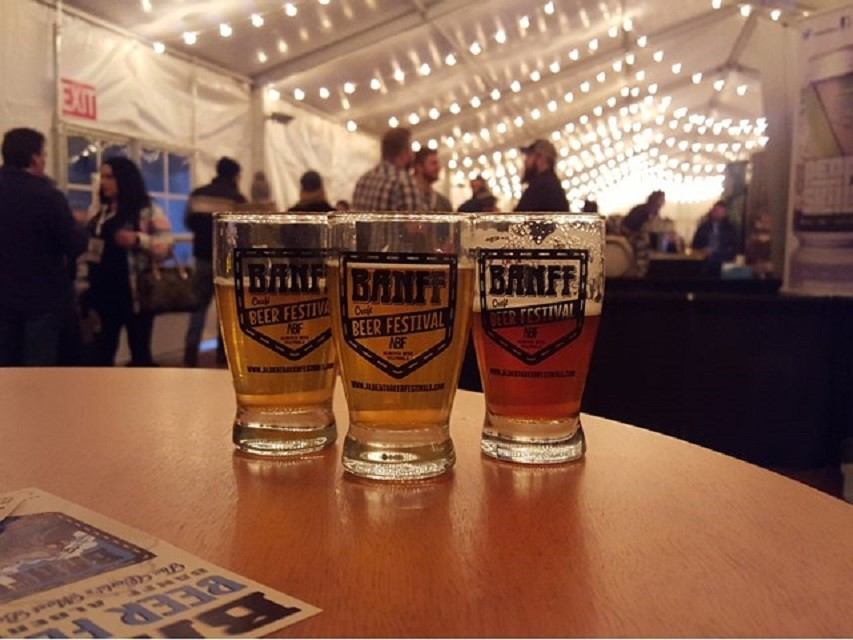 Three beers with Banff Beer Festival labels on a table at a lively event.
