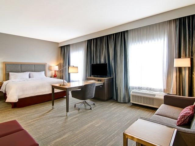 Hotel room at Hampton Grande Prairie with bed, sofa, desk, TV, and large windows.