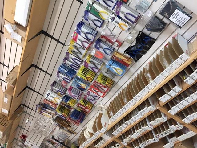 Wall display of packaged hand tools beside shelves of labelled boxes in shop.