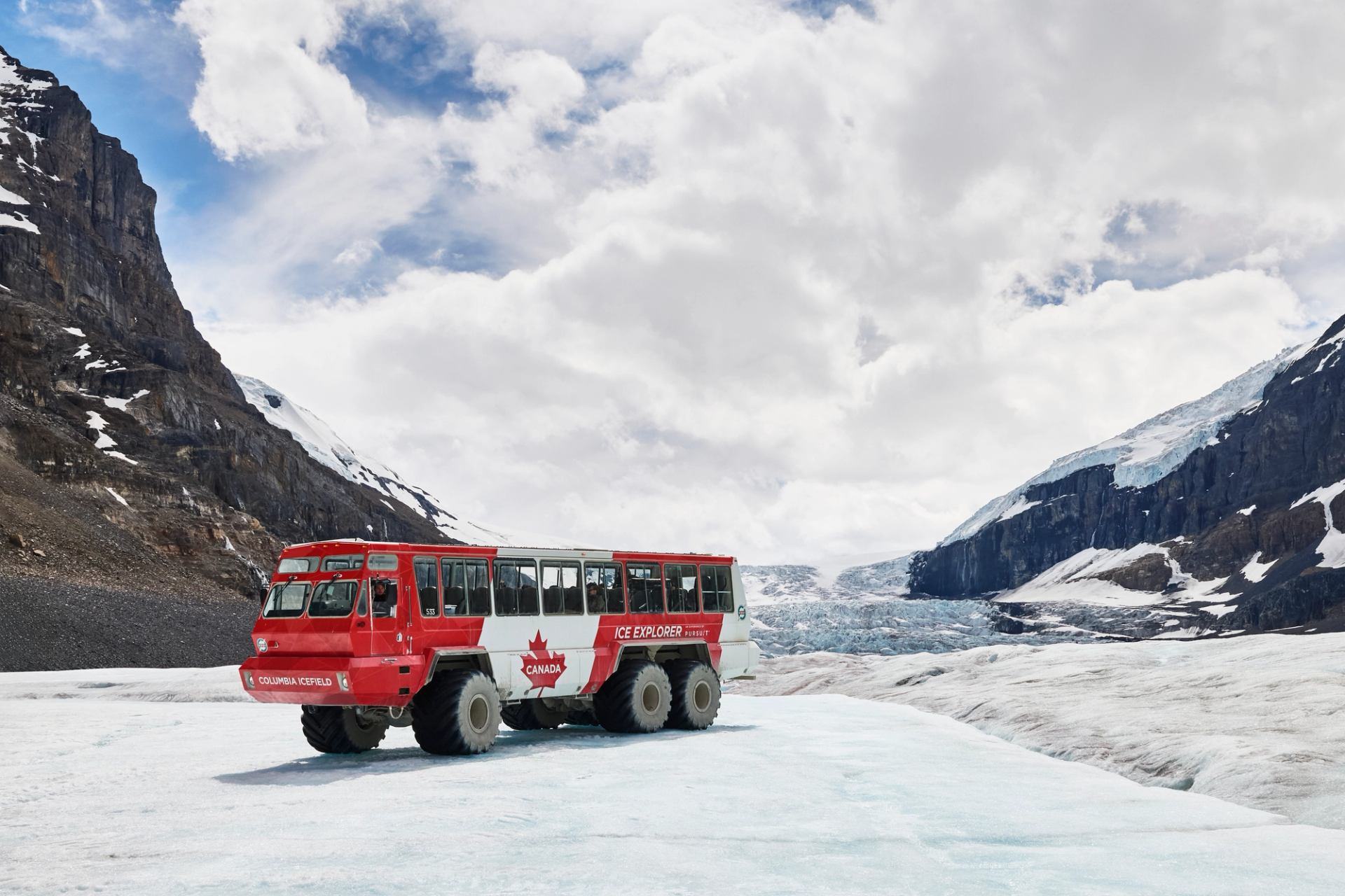 Red Columbia Icefield tour bus on glacier surrounded by rocky, snow-covered mountains.