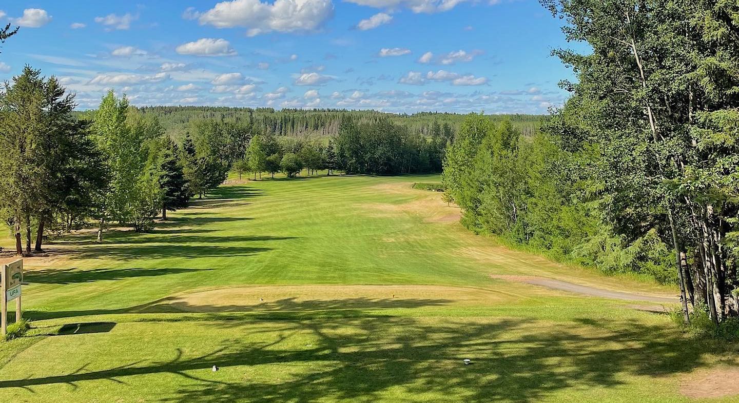 A fairway extends into the distance below a bright blue sky dotted with white clouds.