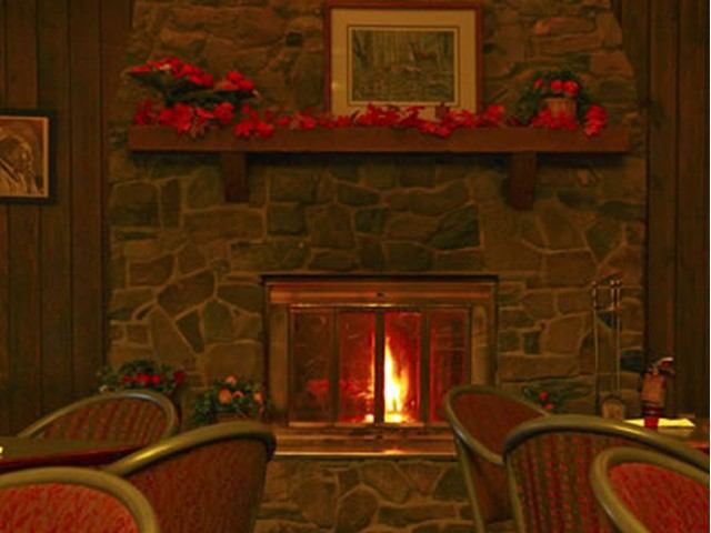 Stone fireplace with a lit fire and seating area inside Nordegg Lodge.