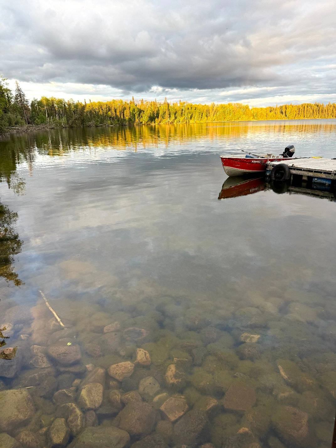 Red boat at a dock on a clear lake with rocks visible under the surface.