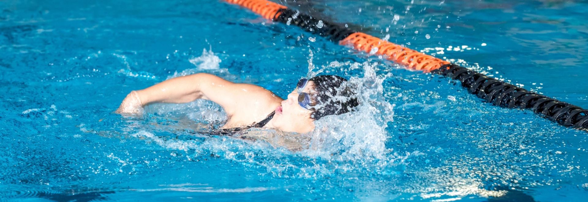 Swimmer wearing goggles and cap does front crawl in lane-marked indoor pool.