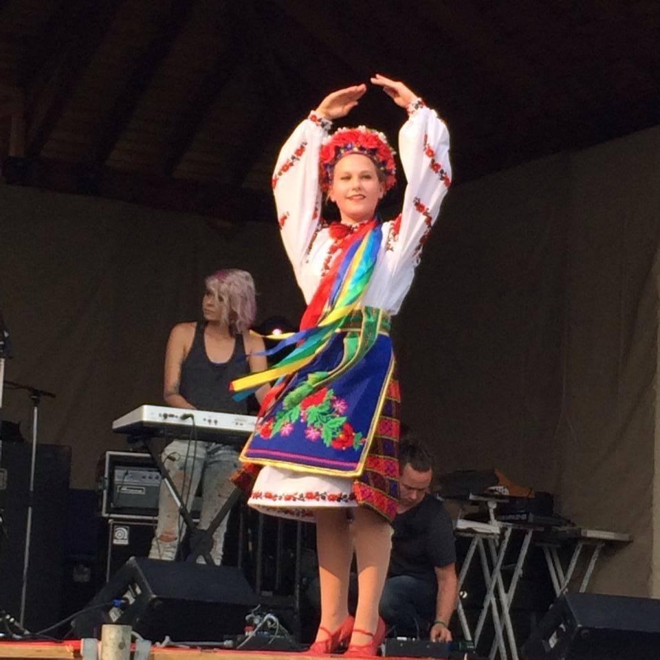Dancer in embroidered folk costume performs on stage with musicians and keyboard behind.