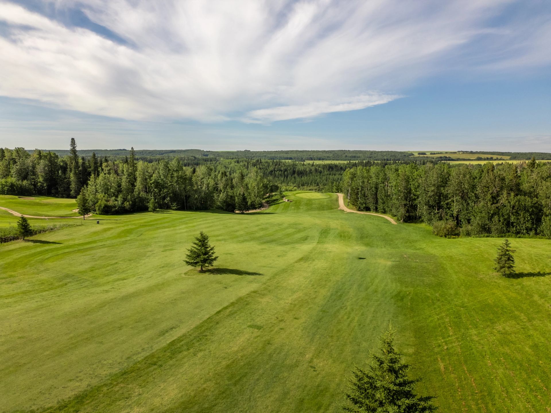 Aerial view of a golf course with green fairways surrounded by dense forests under a partly cloudy sky.