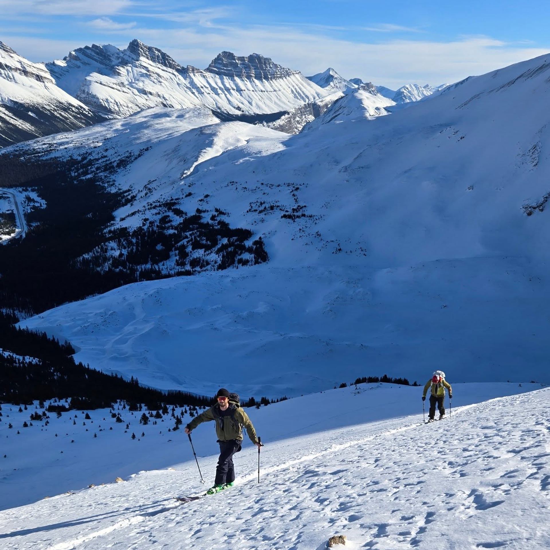 Snow-covered mountains and hikers on skis with poles, overlooking valleys in Banff National Park.