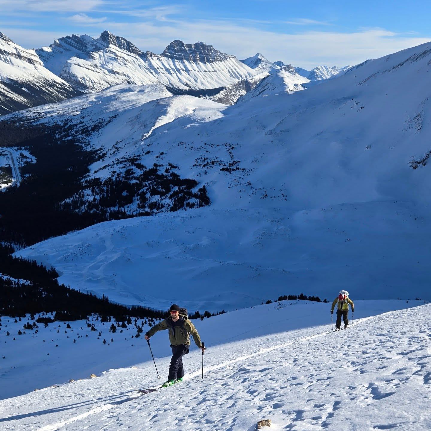Snow-covered mountains and hikers on skis with poles, overlooking valleys in Banff National Park.