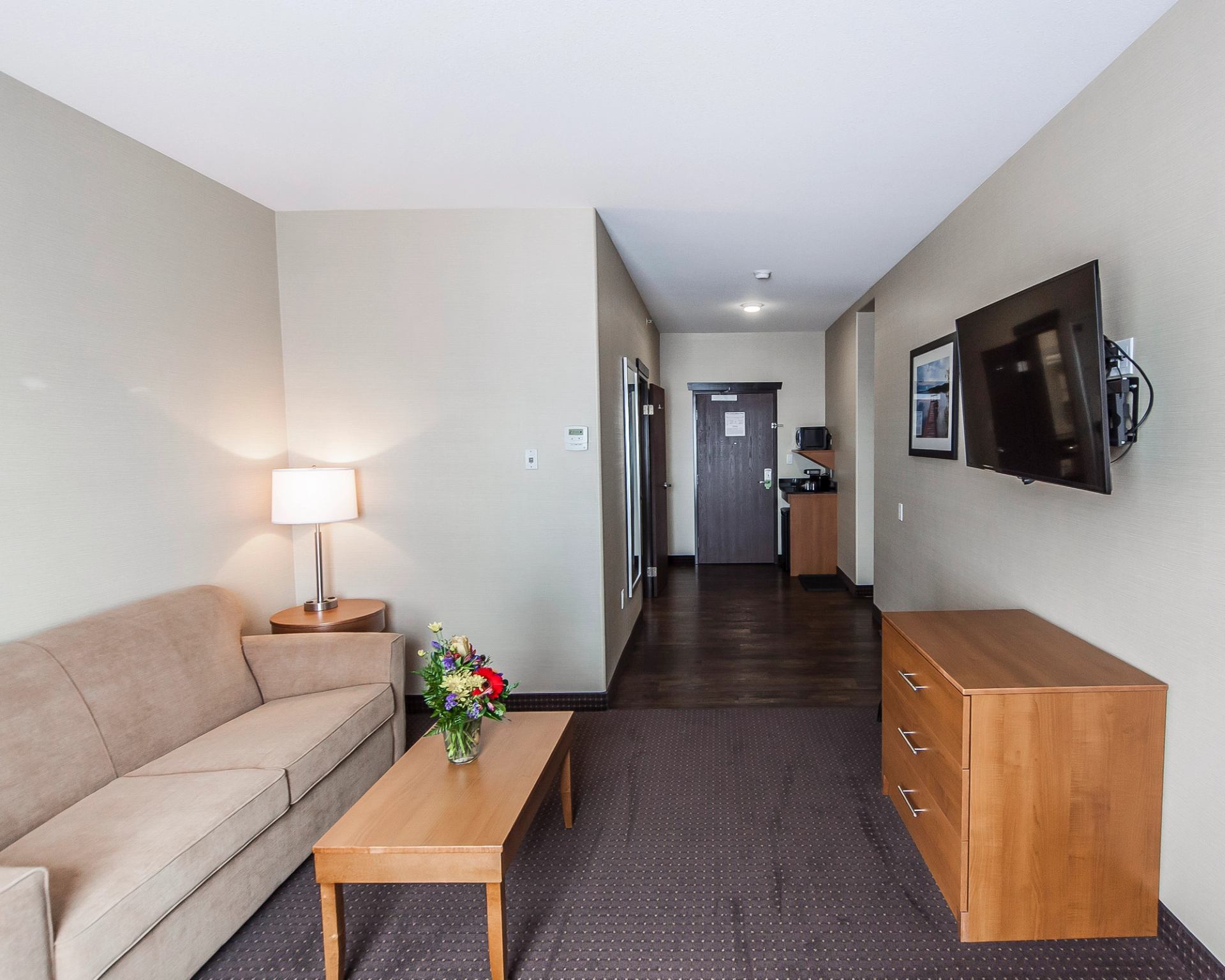 Hotel suite living room with sofa, table, dresser, flat-screen TV, and doorway hall.