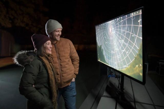 Young couple looking at star chart outside on screen.