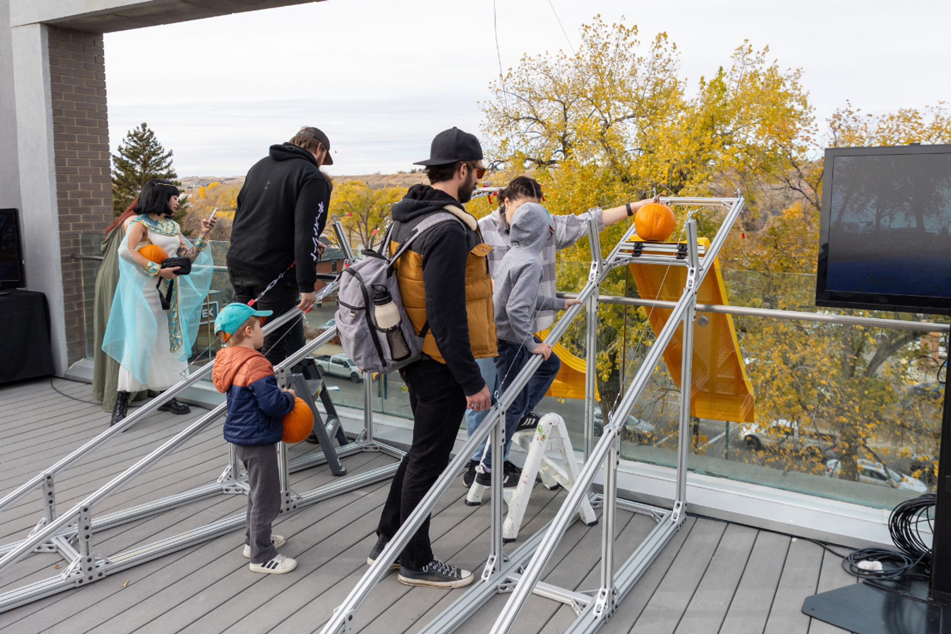 People place pumpkins on metal frames across an outdoor terrace.