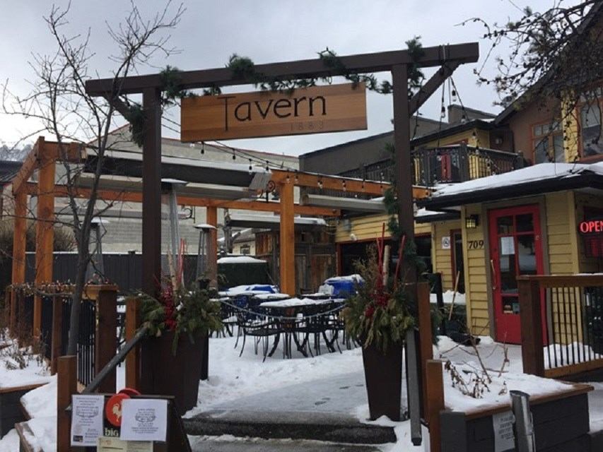 Snow-covered outdoor patio and entrance of Tavern 1883 with wooden pergola and sign.