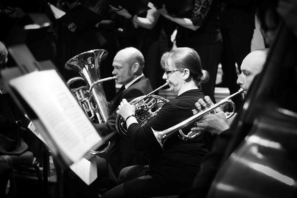 Brass musicians performing in orchestral setting with sheet music in view.