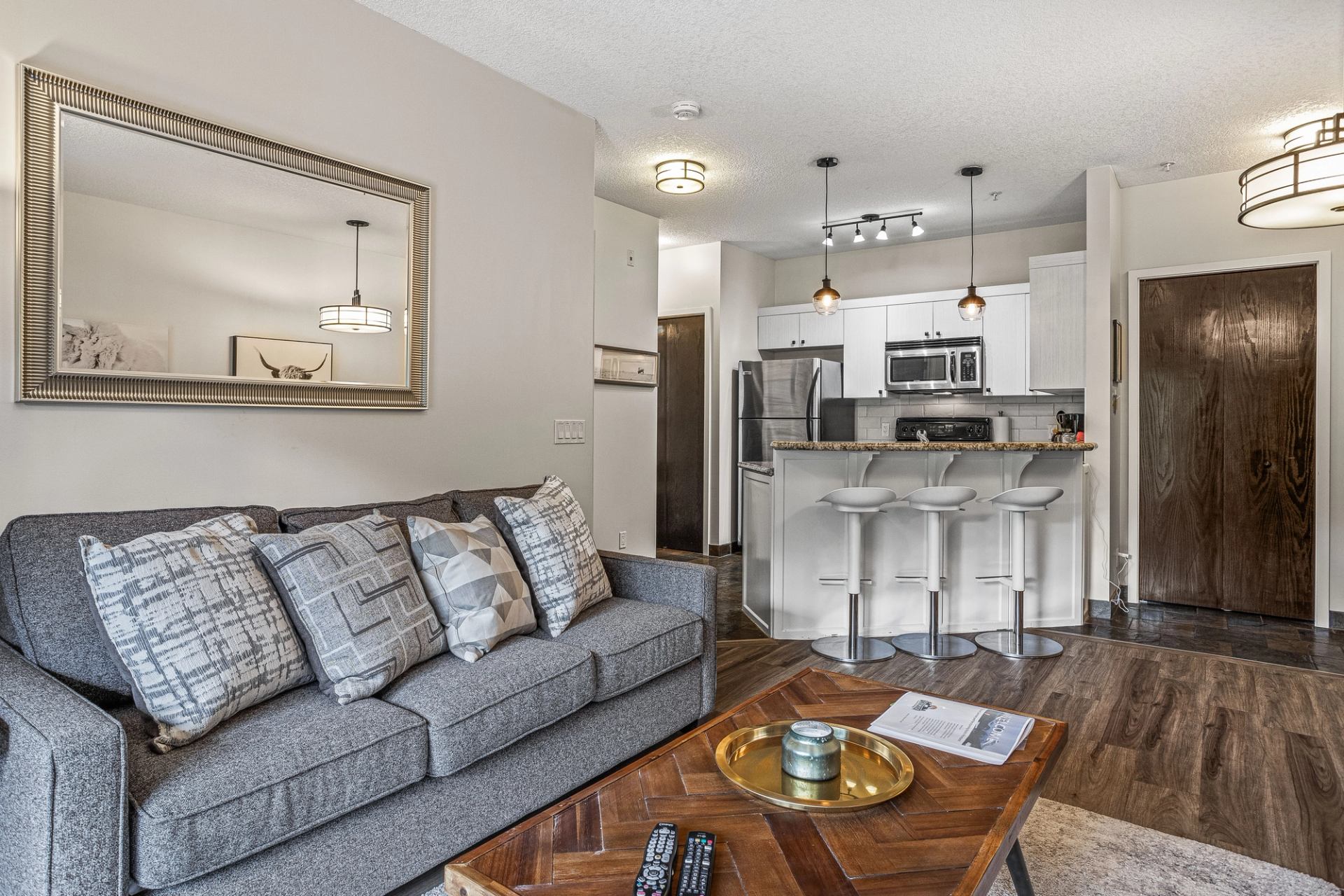 Open-concept living room with grey sofa, wooden table and white kitchen.