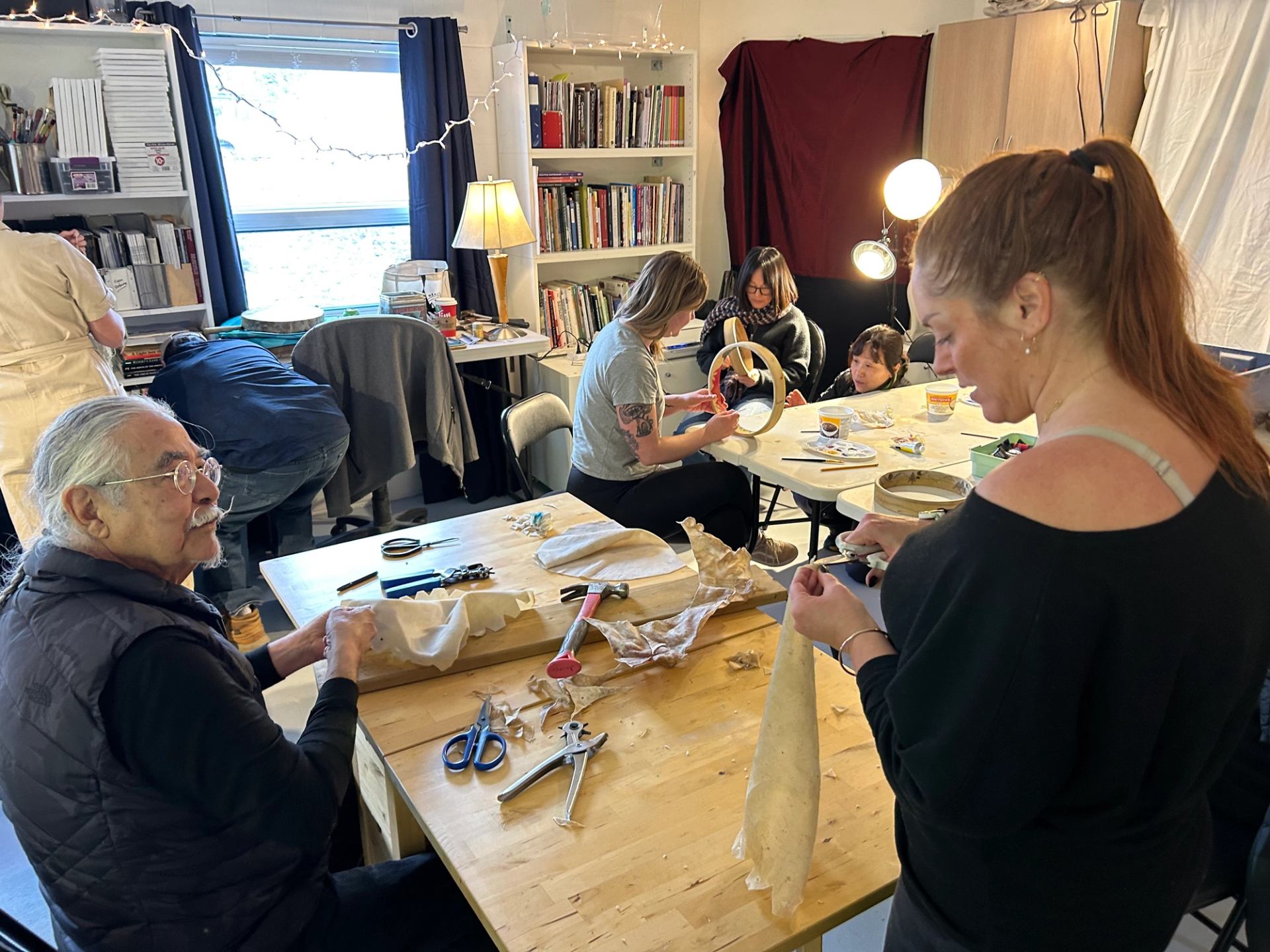 People sit around tables in a craft room, working with fabric and tools.