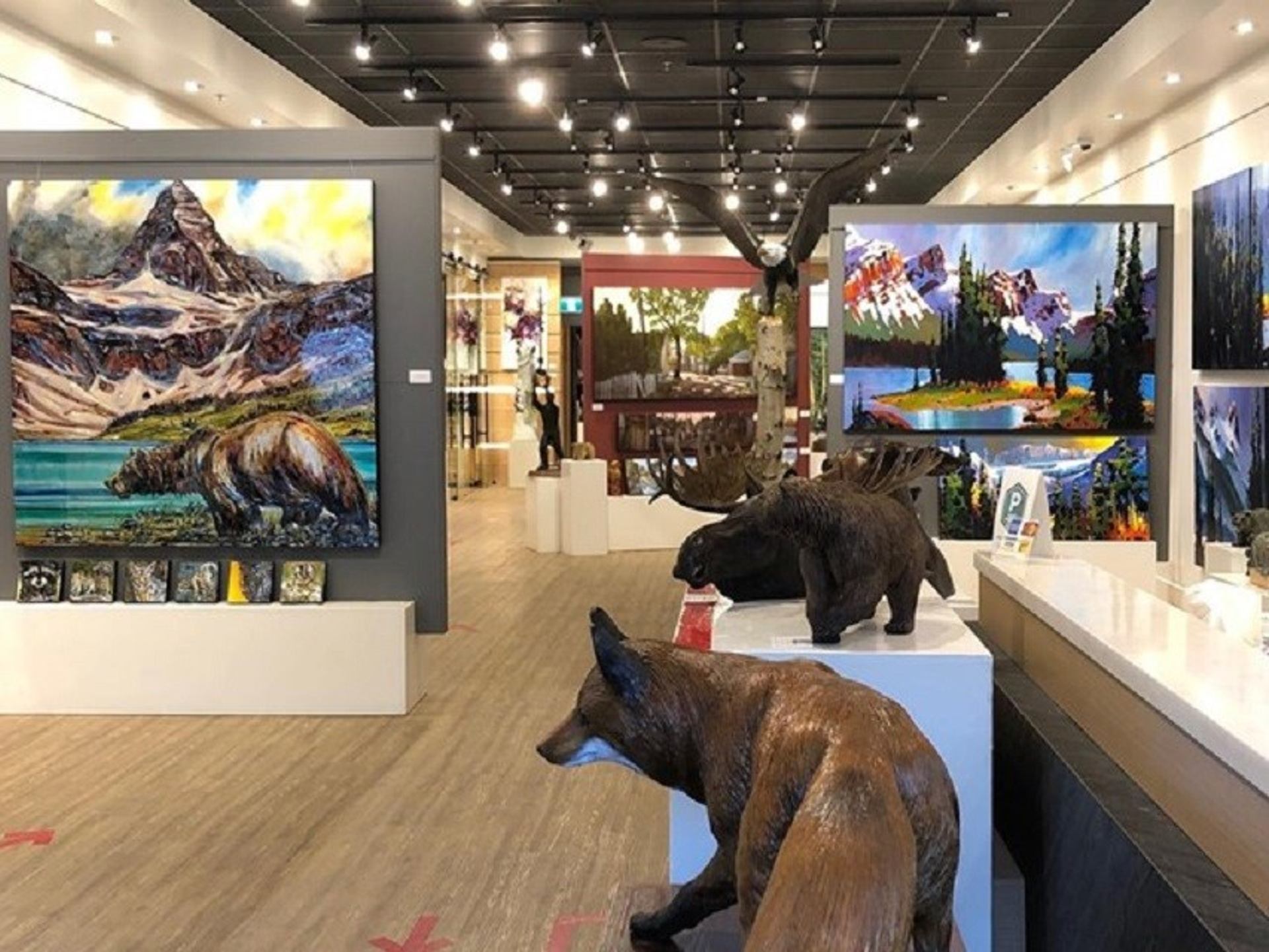 Gallery interior with wildlife sculptures and colorful mountain landscape paintings on display.
