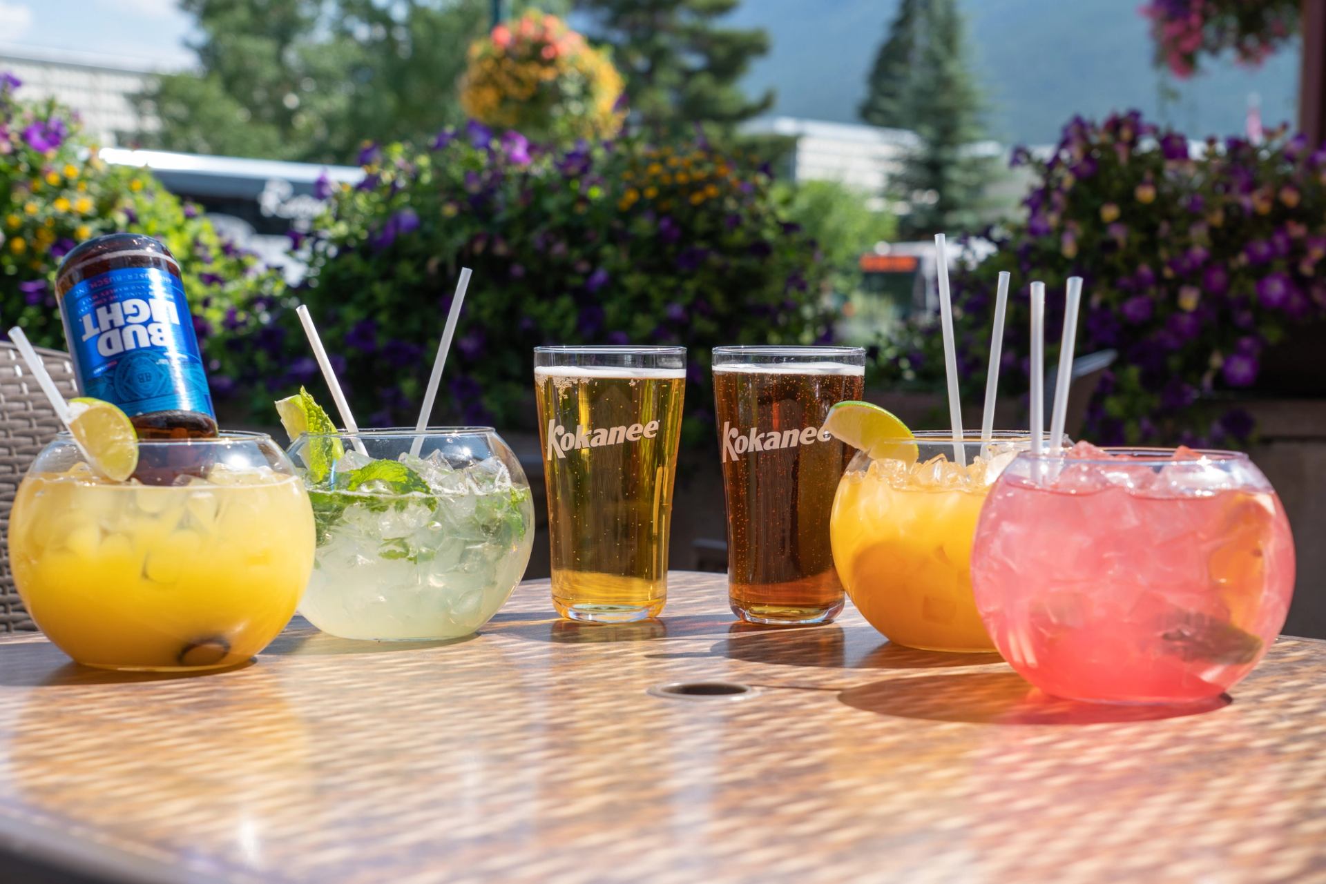 Colorful cocktails and beer served outdoors with floral garden backdrop.