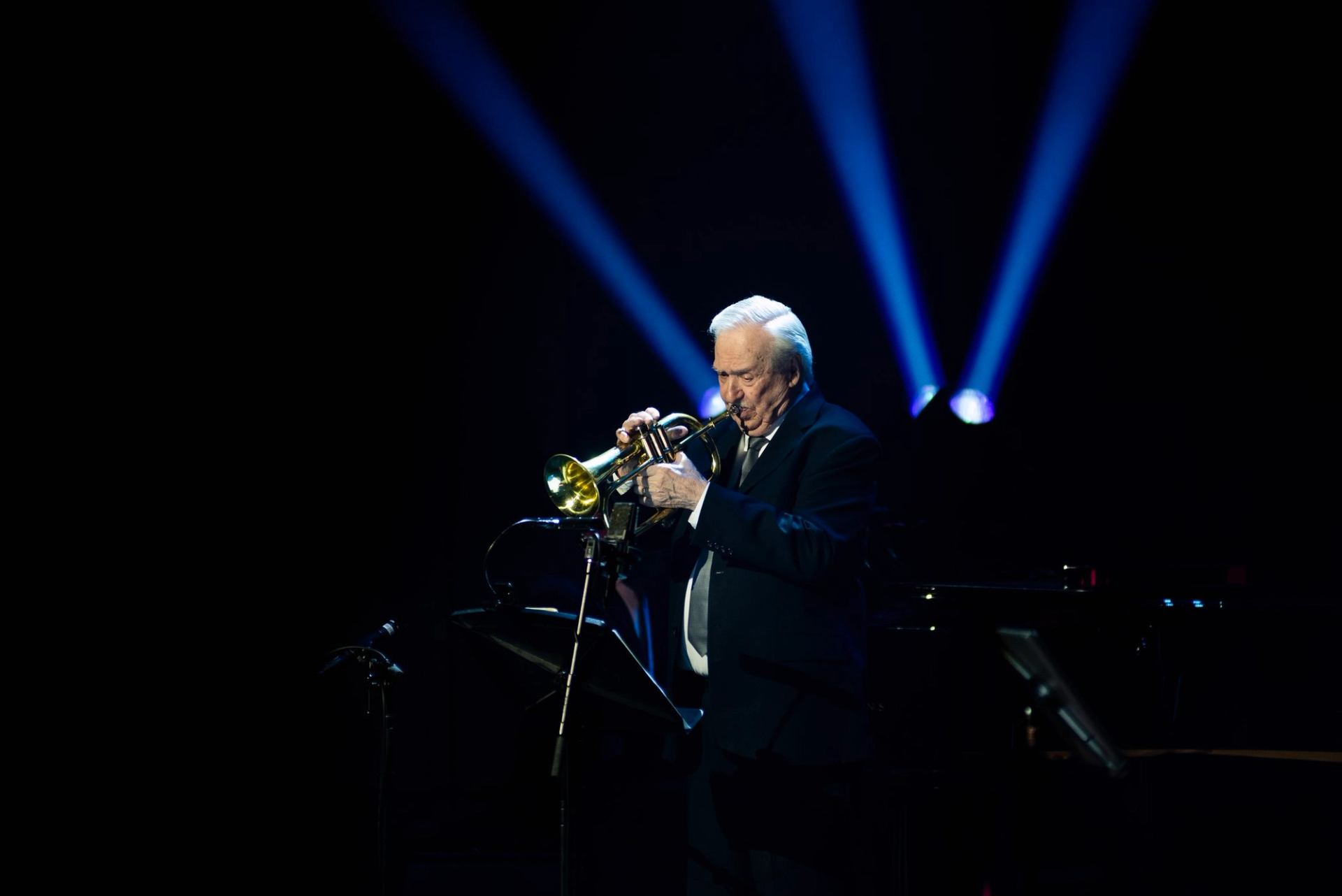 Trumpeter performing under blue spotlights on a dark stage.
