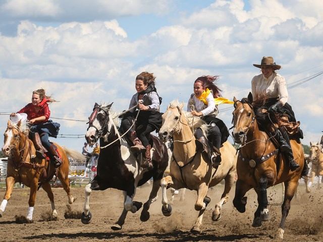 Group of riders galloping side by side on horses during a fast-paced race in the rodeo arena.