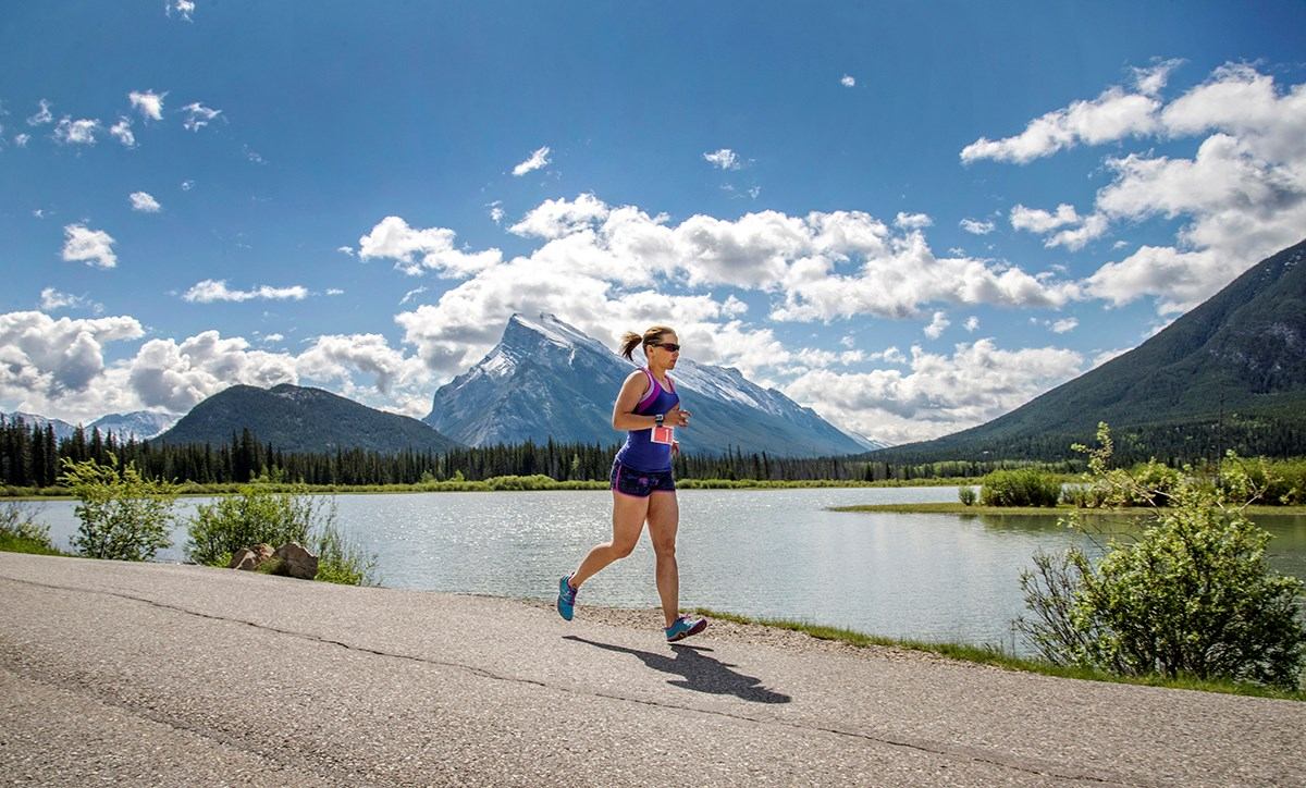 Runner on lakeside path with mountains and greenery.