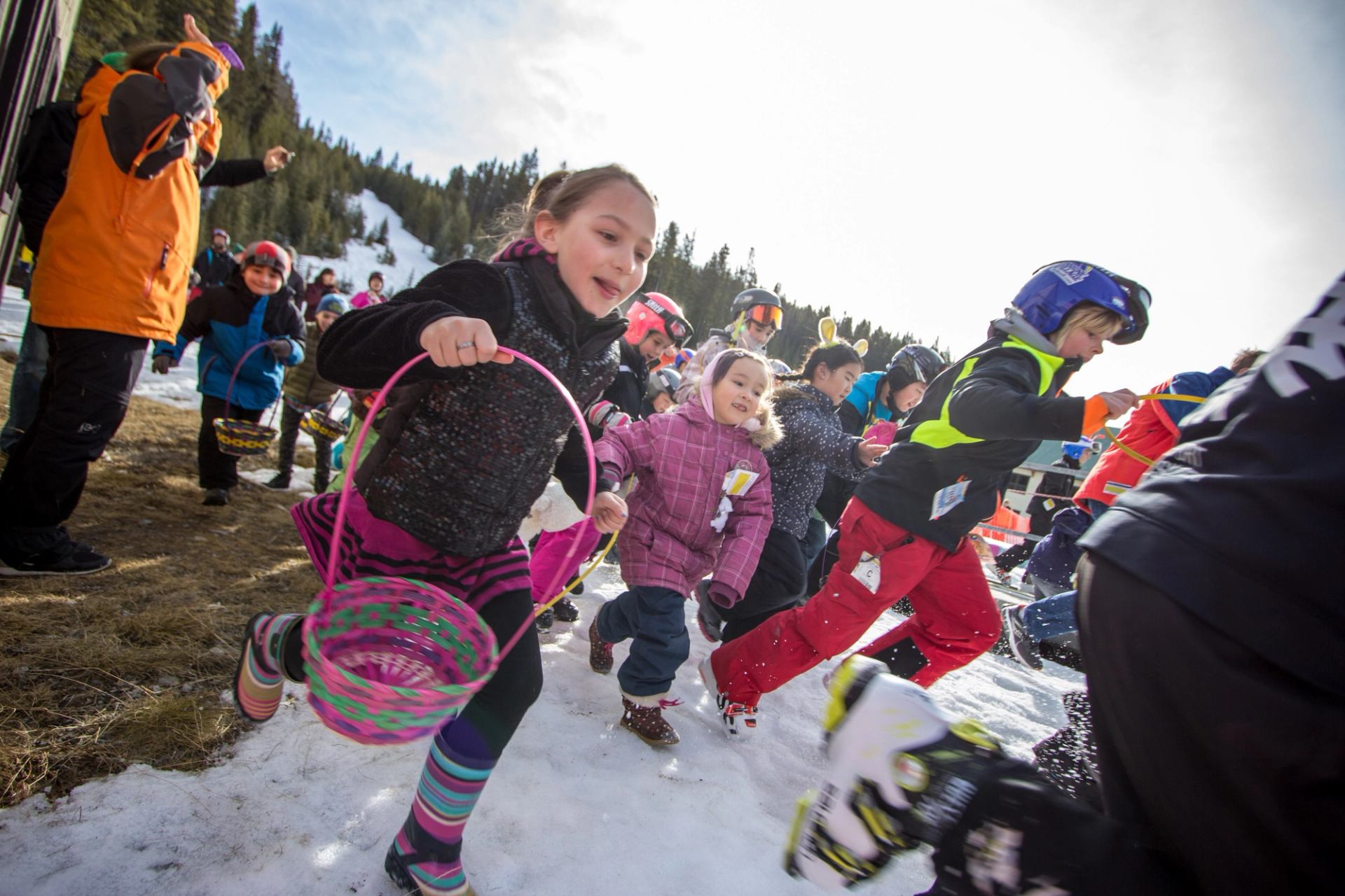 Kids dash through snow with baskets during Norquay Easter egg hunt.