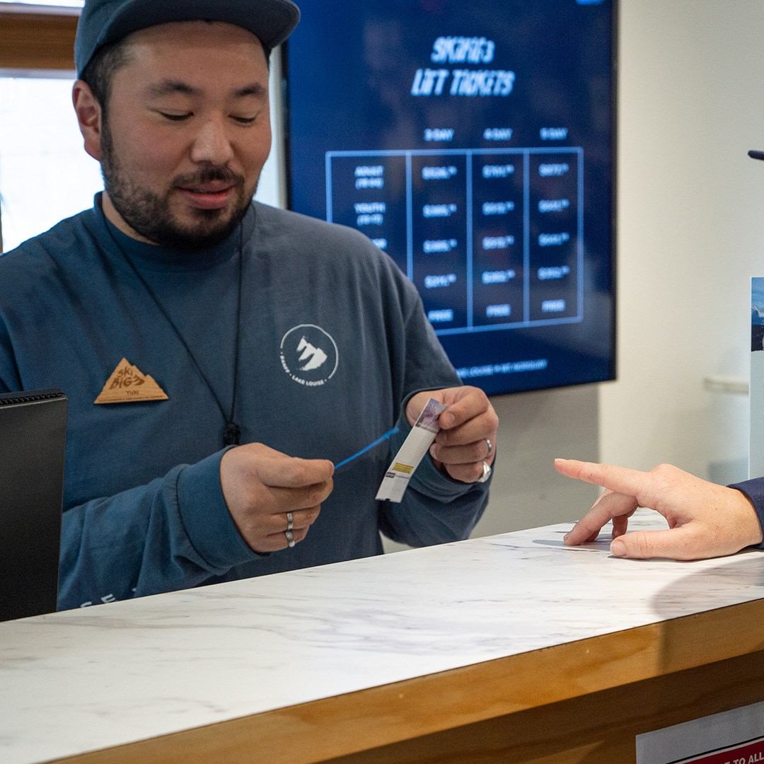 Person holding a badge at SkiBig3 counter with lift ticket options on screen.