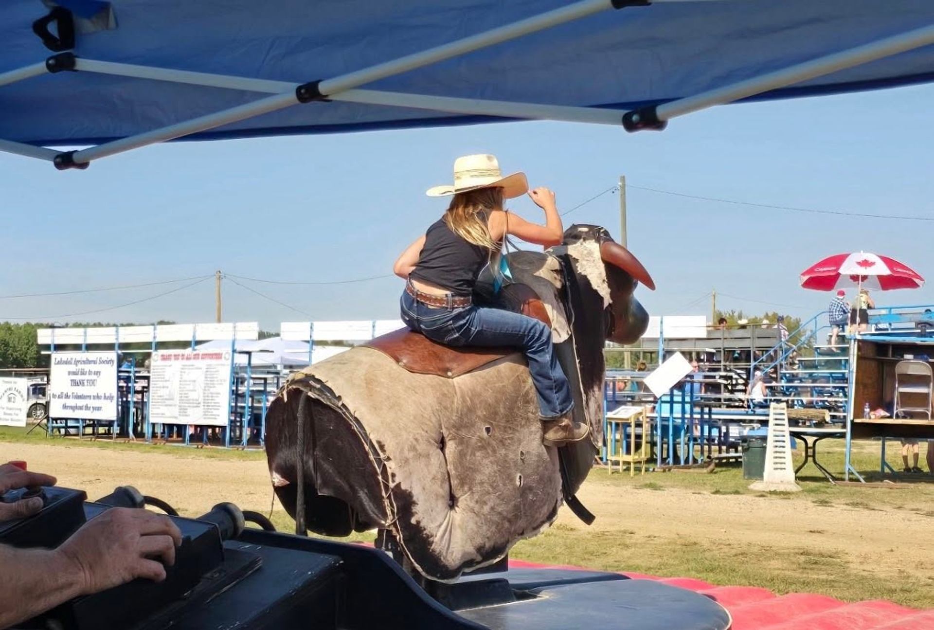 A rider holds on to a mechanical bull during an outdoor community event at the fairgrounds.