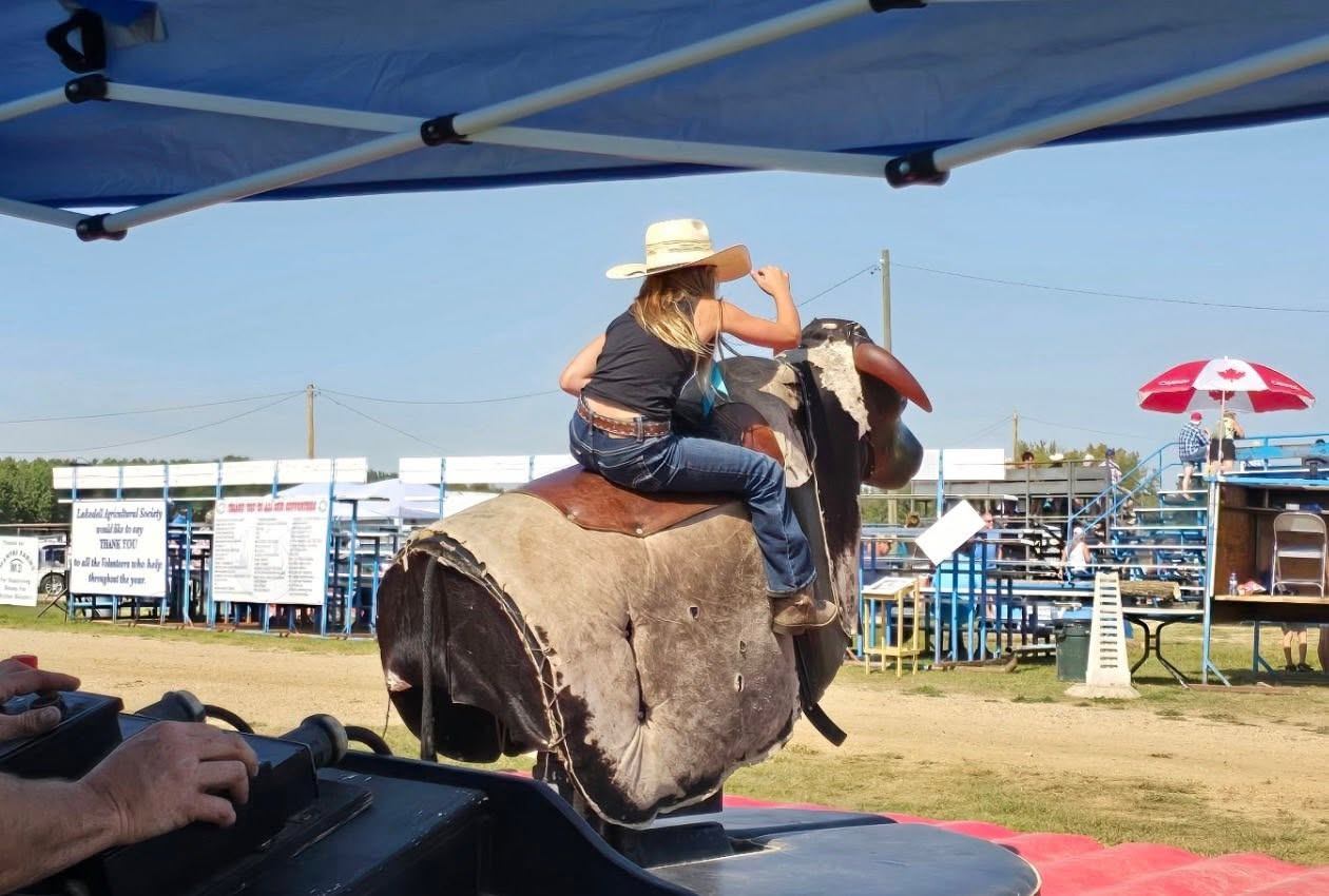 A rider holds on to a mechanical bull during an outdoor community event at the fairgrounds.