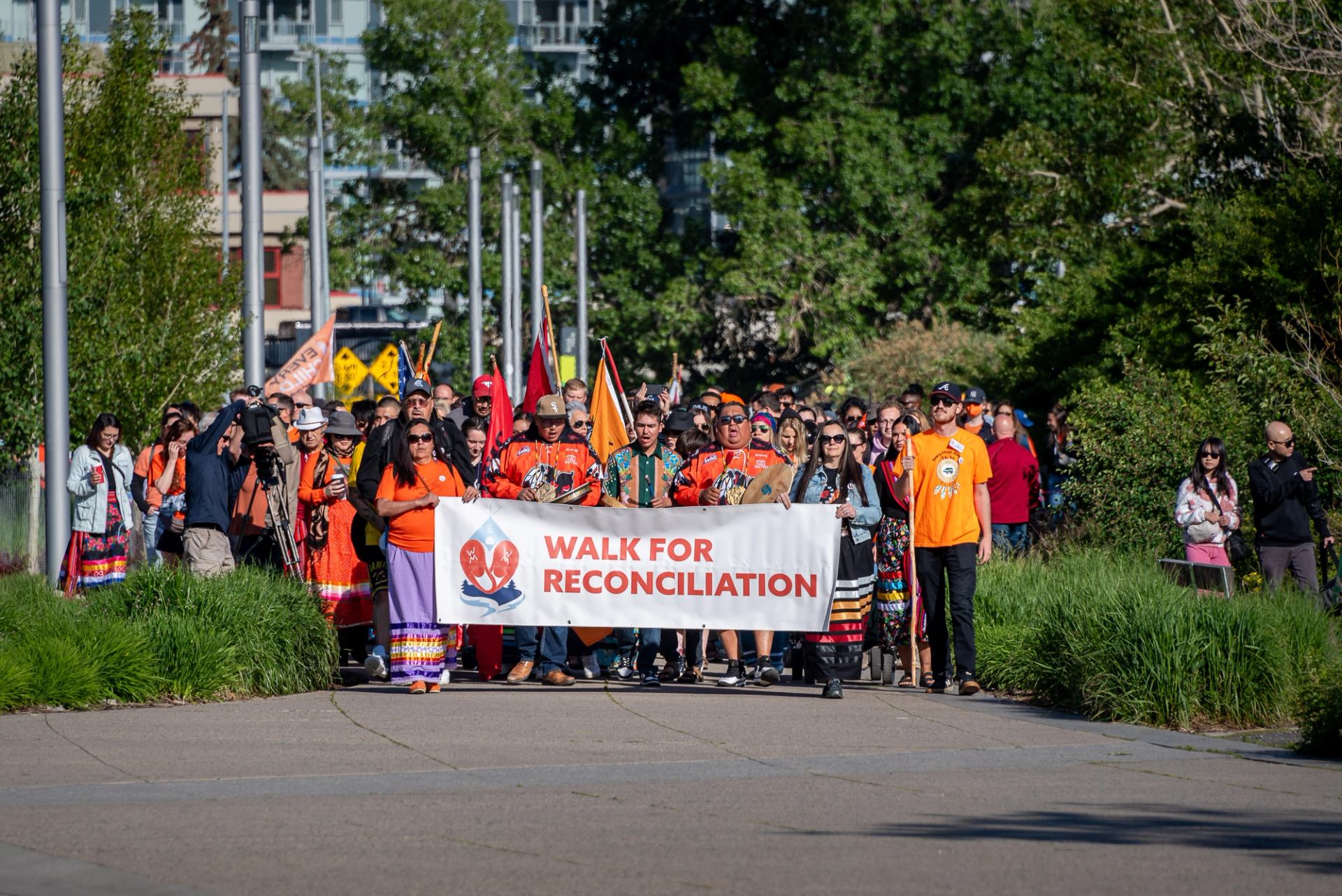 Crowd marching with a banner reading “Walk for Reconciliation” in downtown Calgary park.