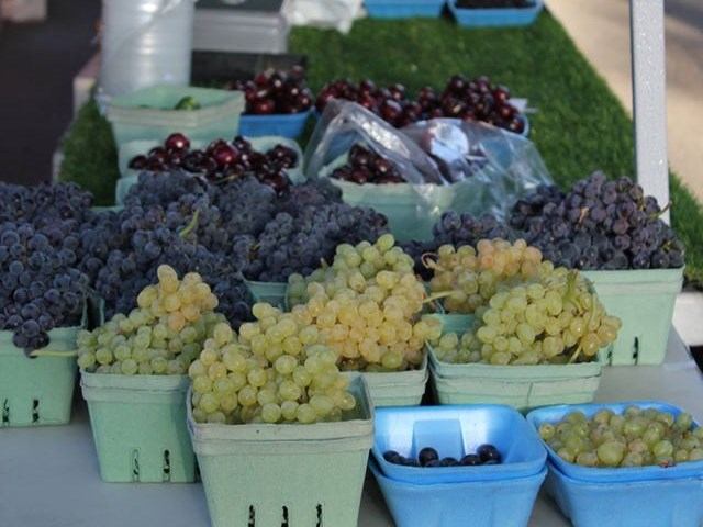 Green and purple grapes arranged in baskets on a vendor table