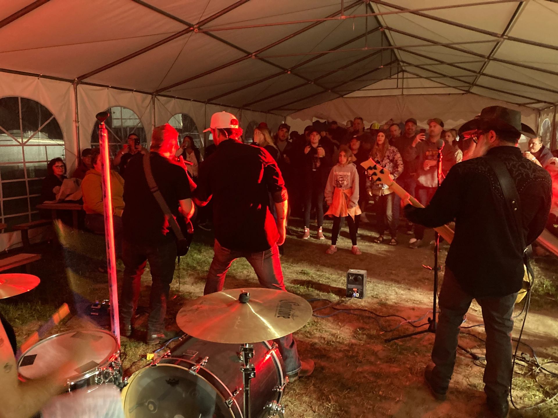 Band performs under a tent with red stage lighting as crowd watches closely.