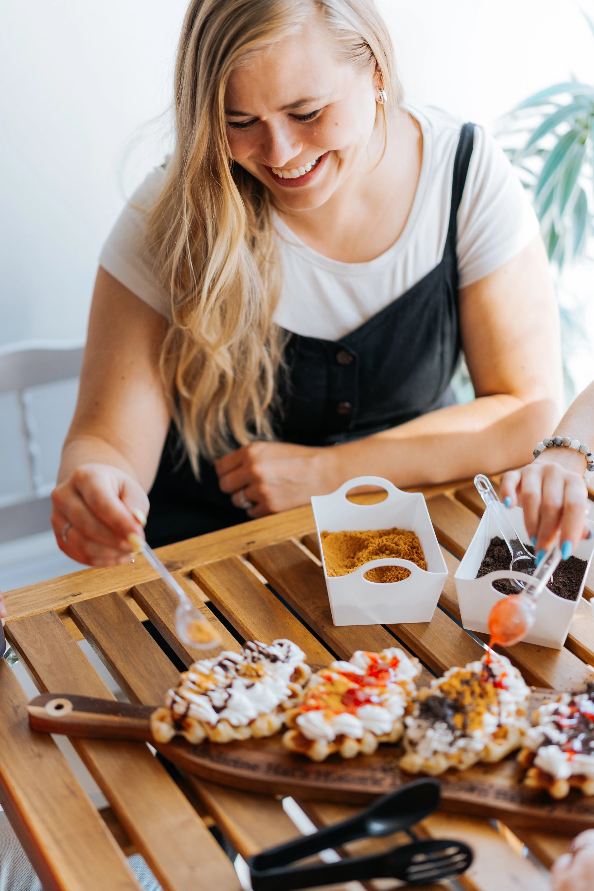 Hands adding sauces and toppings to assorted pastries on a wooden table during a bakery tour.