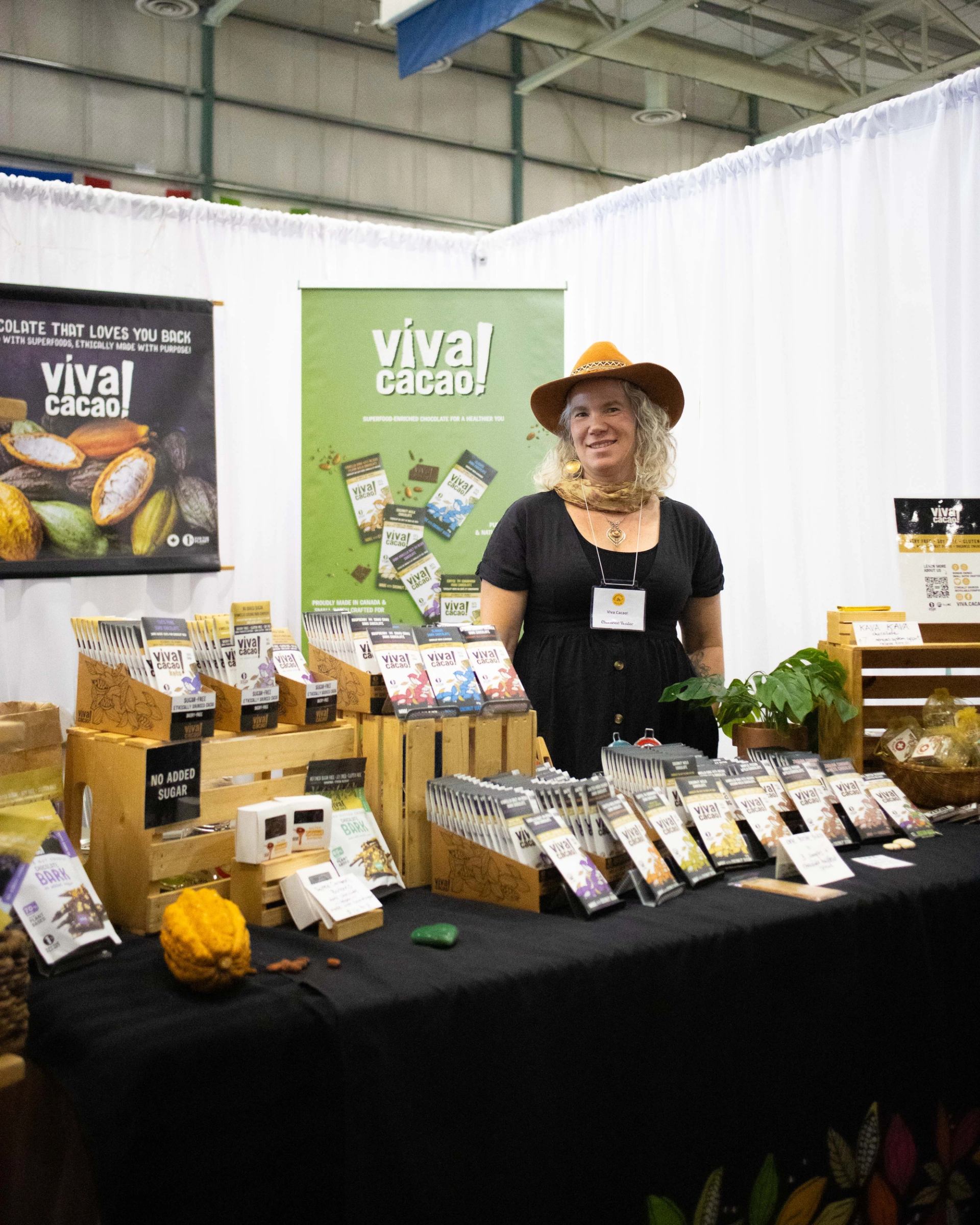 Vendor stands behind Viva Cacao booth displaying assorted chocolate bars and product samples.