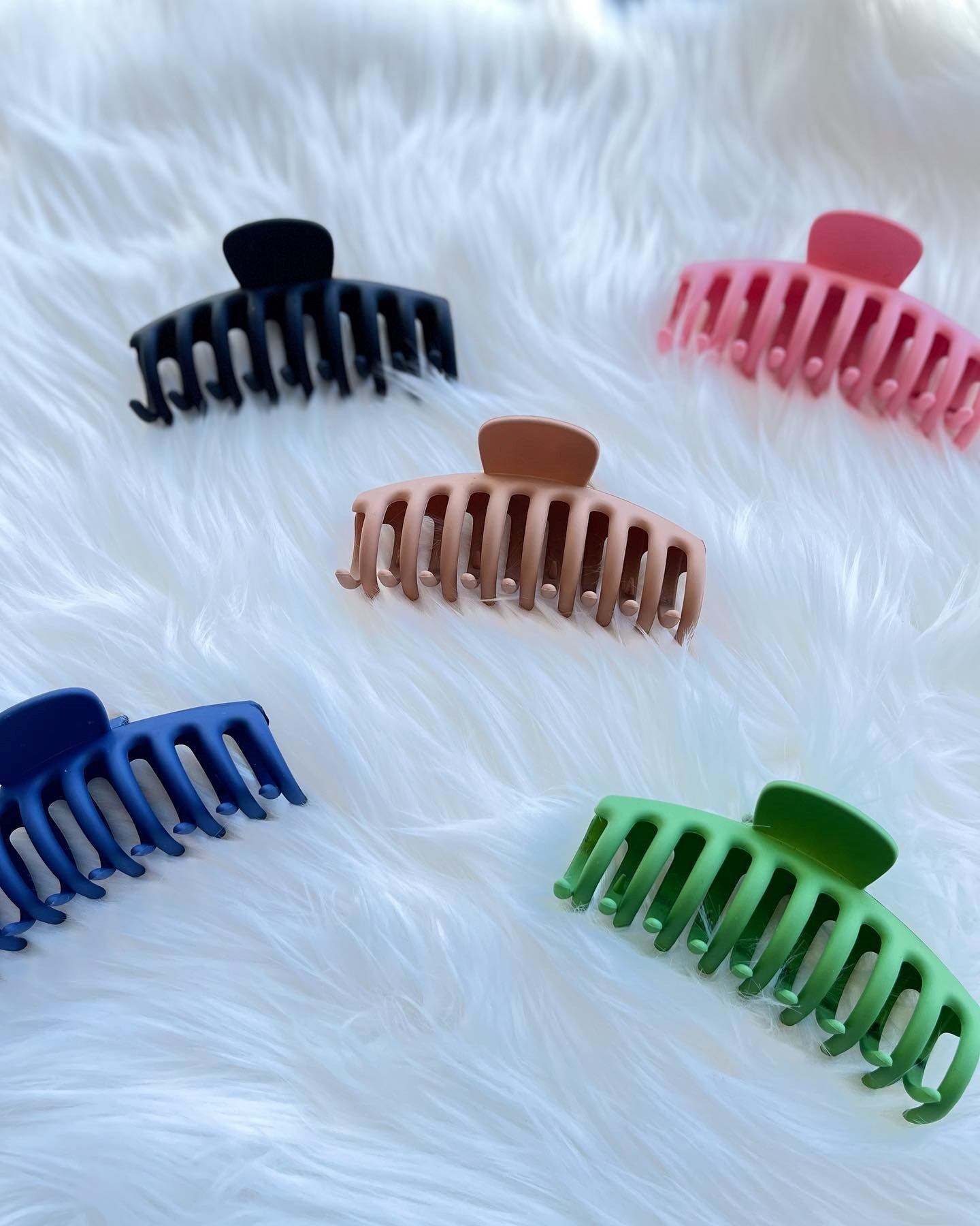 Colored plastic hairbrushes on white fabric background, five brushes visible.