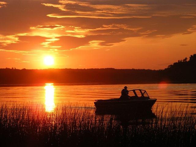 Boat on calm lake at sunset with orange sky and reflections at Coal Lake South Park.