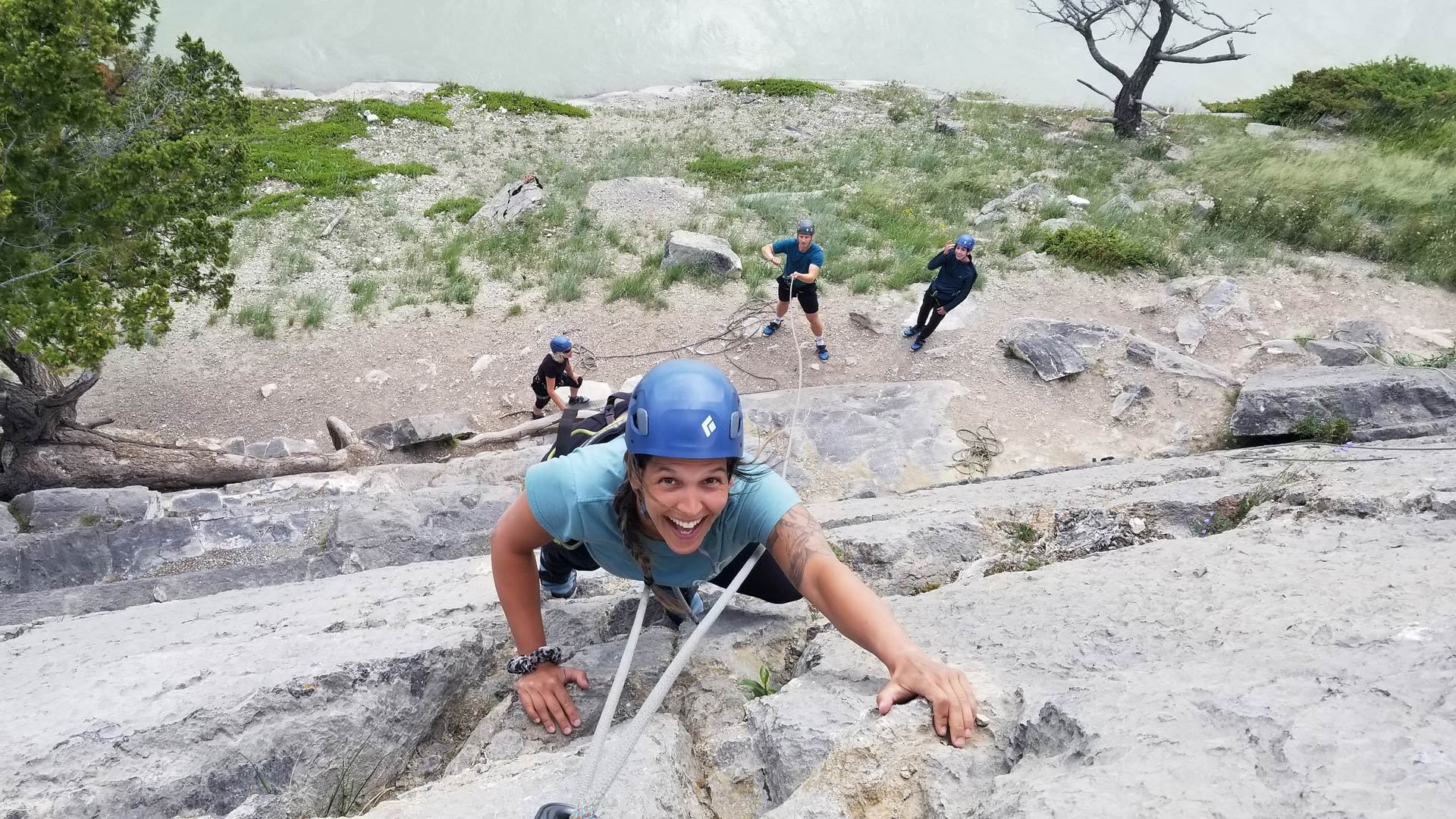 Rock-climbing group on rope, wearing helmets, on steep rocky ledges with boulders.